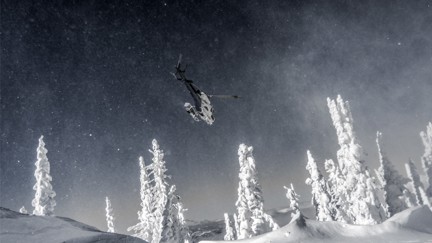 A Helicopter flying over head in heavily snow covered forested mountain.