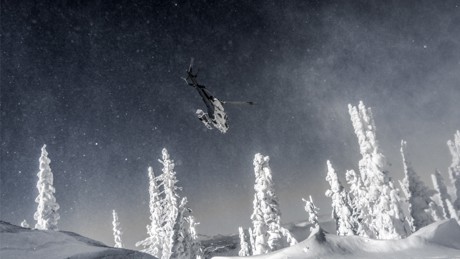 A Helicopter flying over head in heavily snow covered forested mountain.