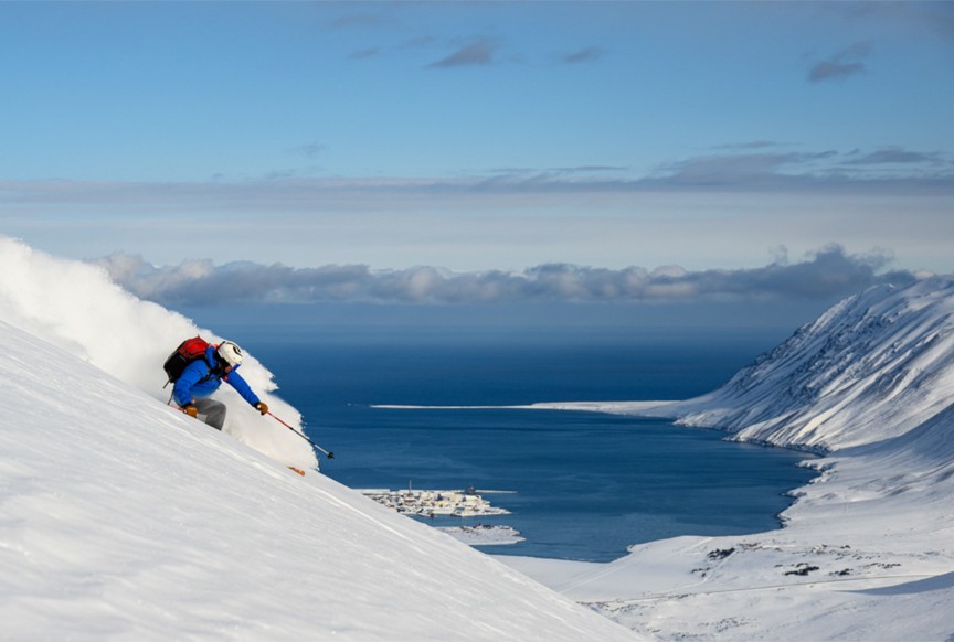 A skier headed downhill on a mountain with a view of the ocean behind.