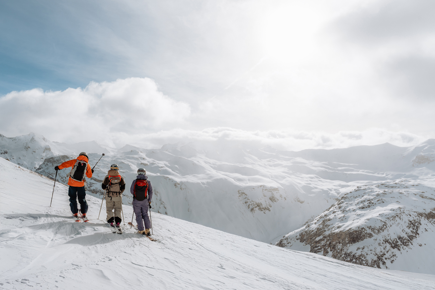 A group of people carrying their skis over a mountain crest in the snow in the evening.