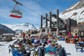 A large group of skiers hanging out at the bottom of a ski lift at a lodge.
