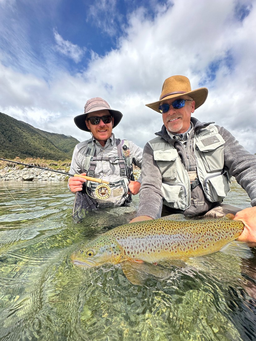 Two fishers holding a large trout in a river.