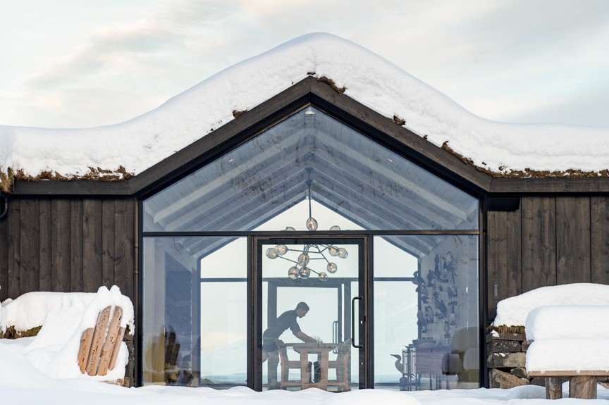 A person setting up a table in a glass dining room.