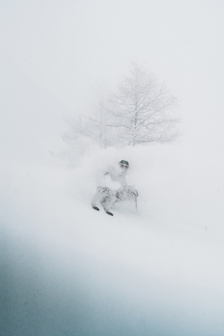 A skier in a cloud of snow headed down a near vertical slope.