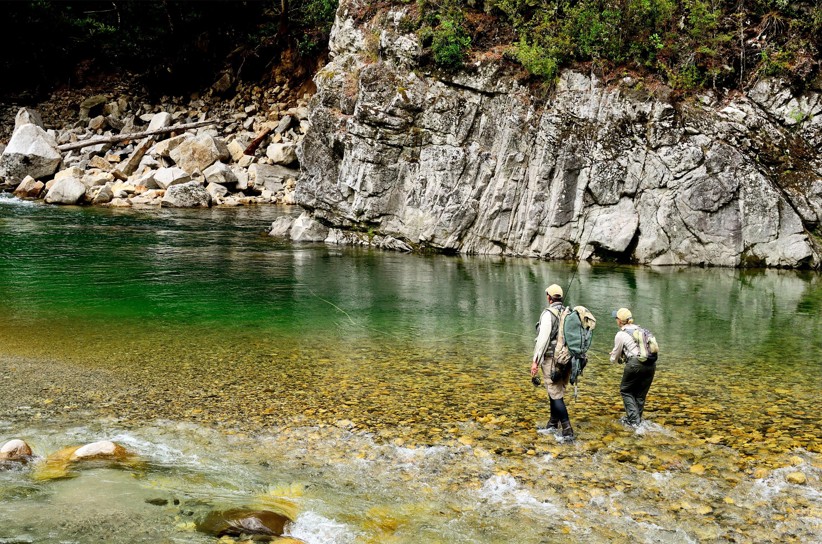 Two people wearing waders fly fishing in the middle of Owen River.