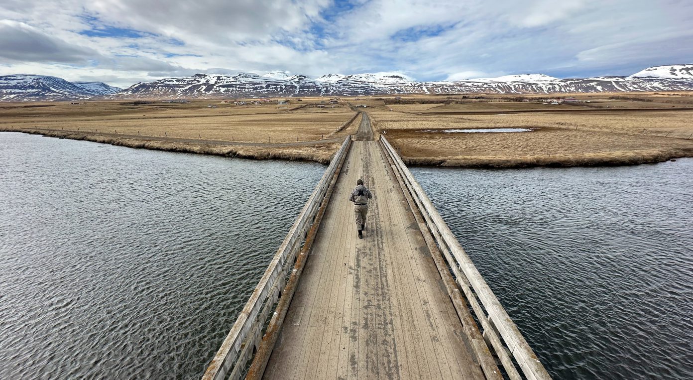 An angler walks across a bridge in Iceland.