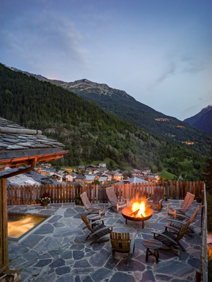 A patio with a fire pit overlooking a mountain valley and small village.