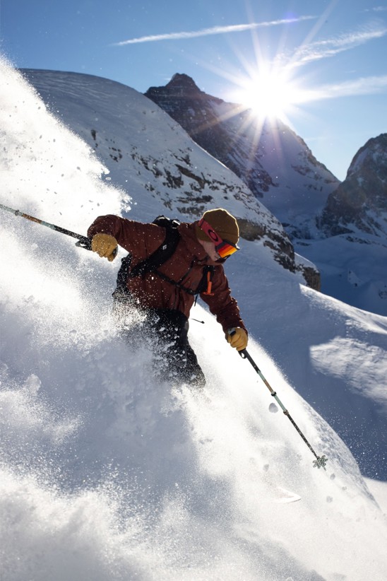 A skier in a cloud of snow headed down a near vertical slope.