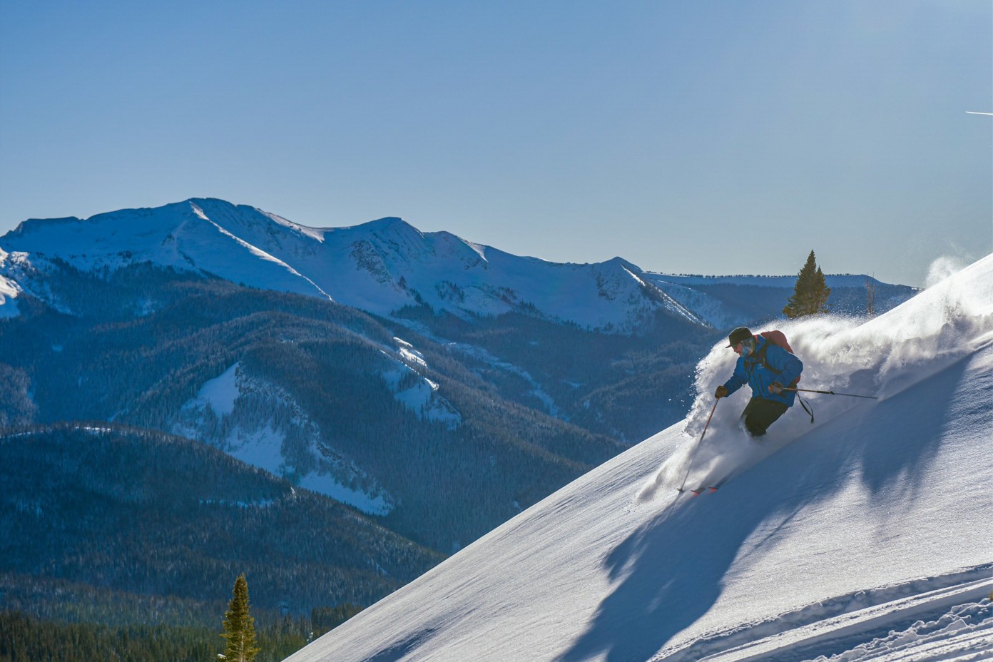 A skier carving near the top of a mountain with a view of a mountain range.