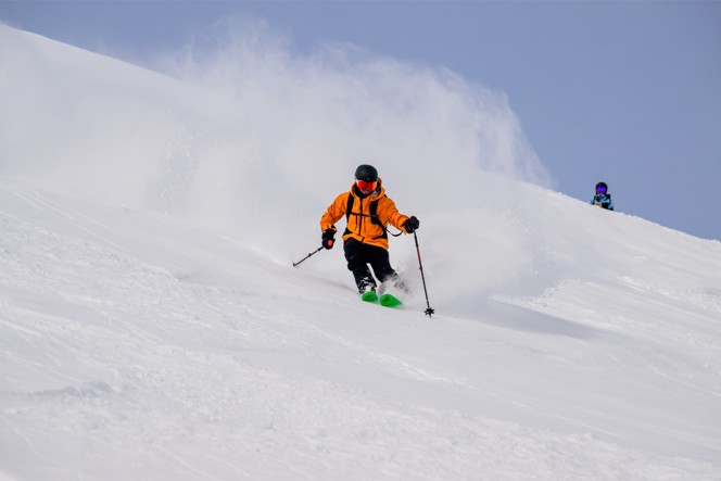 A skier in a bright orange coat headed down a mountain.