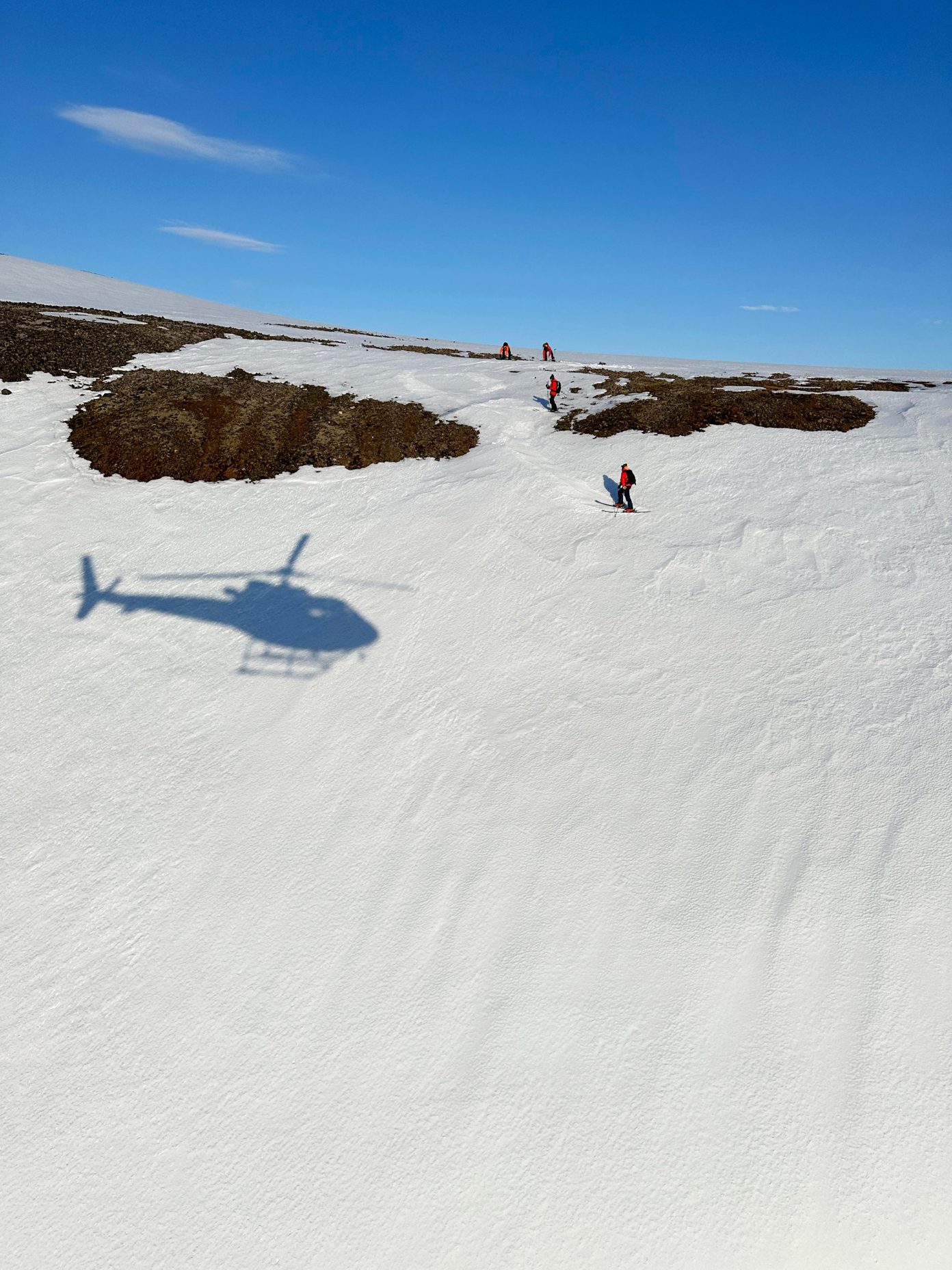 A group of skiers assess their descent in the shadow of a helicopter.