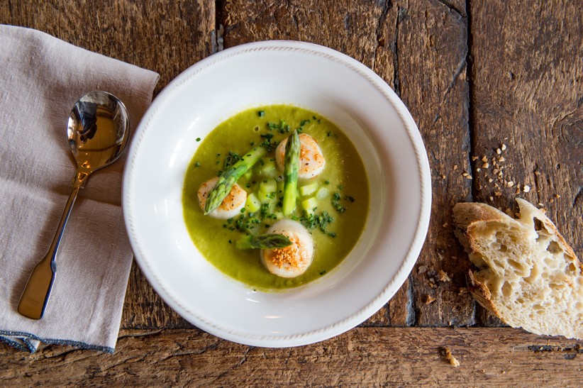 A bowl with cooked fish and asparagus with a side of fresh bread.