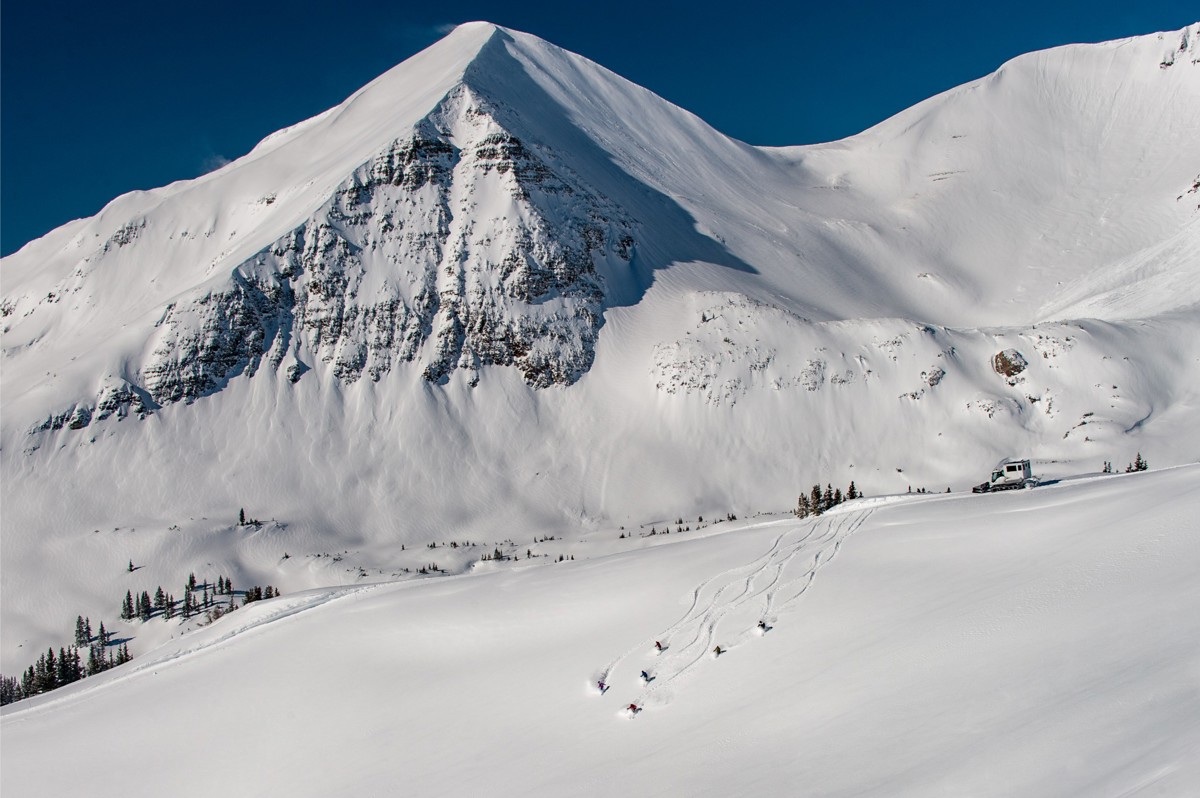 Group of people skiing atop a tall snow covered mountain.