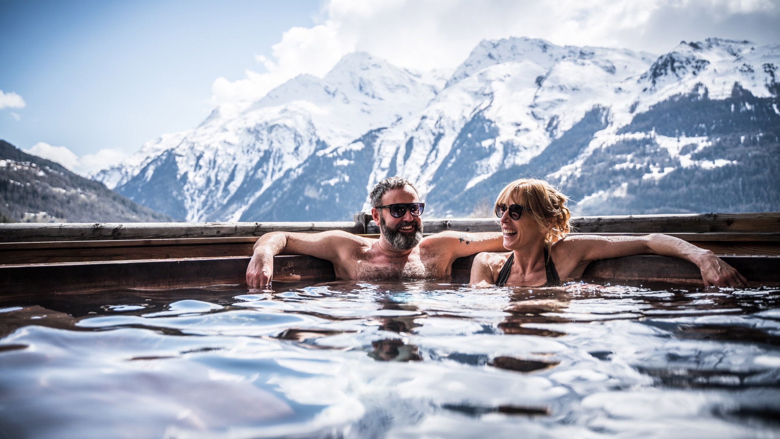 A group of people in an outdoor hot tub with a view of the snow covered alps.