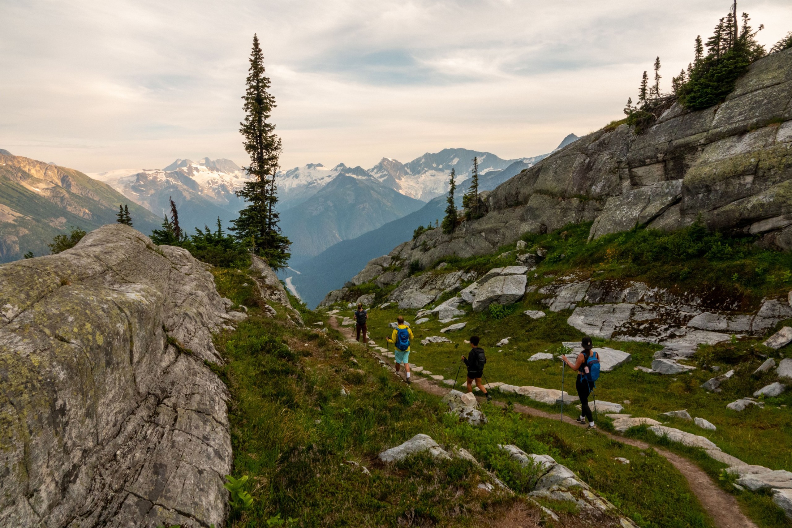 A group of people hiking through a rocky pass atop green mountain range.